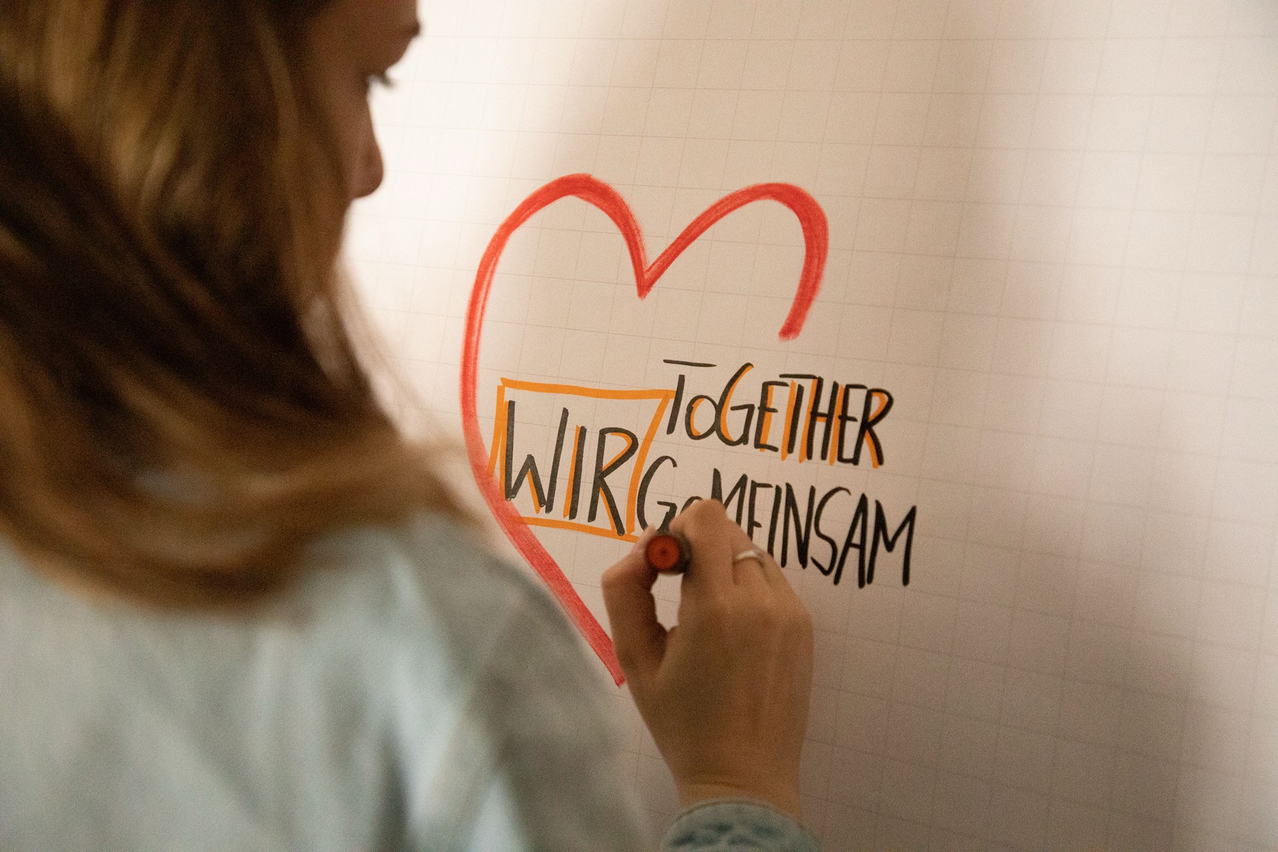 Mensch zeichnet ein rotes Herz mit der Aufschrift „Wir gemeinsam“